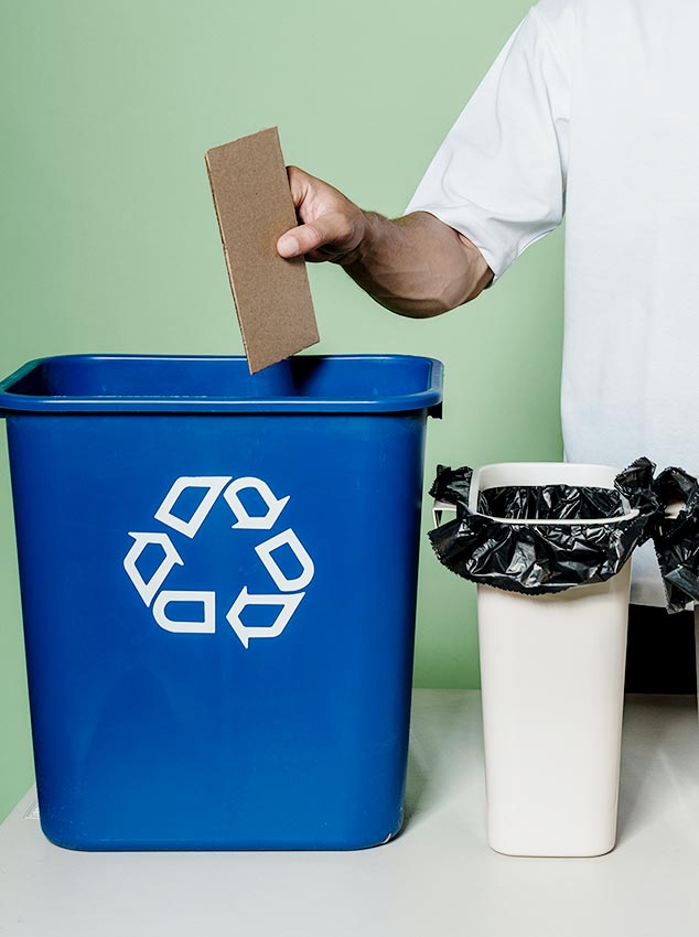 Someone places a scarp of cardboard in a blue recycling bin