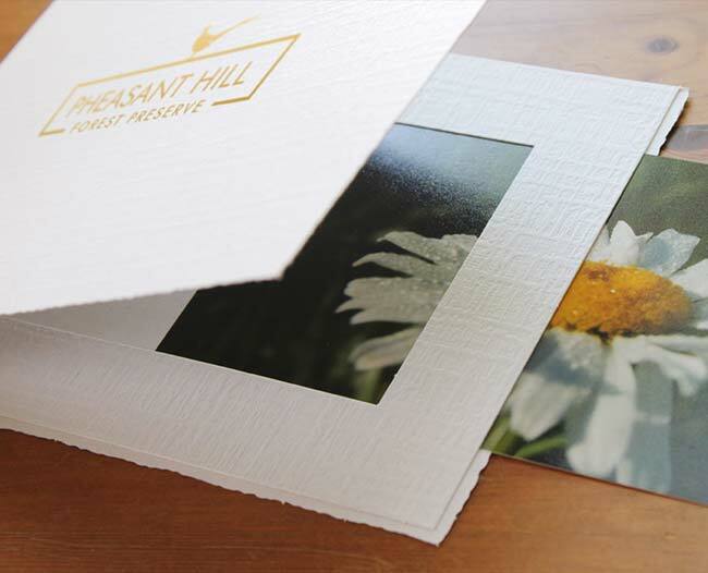 White portrait folder with gold foil logo imprint on the front cover and photo being inserted into the window frame border.