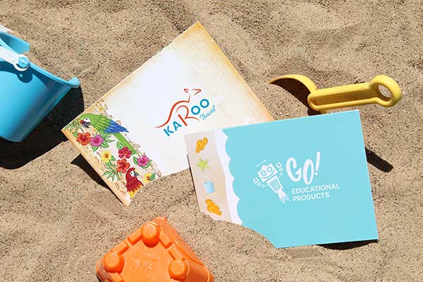 Summer-themed photo folders sit on a sandy beach by colorful toys