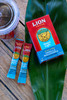 Lion Vanilla Macadamia Instant Coffee Box with two instant coffee sticks on top of a green leaf