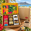 Lion, Royal Kona, and Hawaiian Isles coffee bags displayed on a woven mat with Diamond Head and palm trees in the background, alongside a hibiscus flower and a cup of coffee