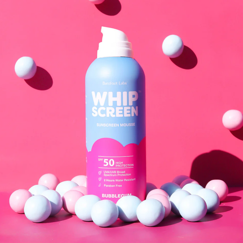 A bottle of Barefoot Labs Whip Screen Sunscreen Mousse, SPF 50, in bubblegum flavor, surrounded by pastel pink and blue balls on a pink background.