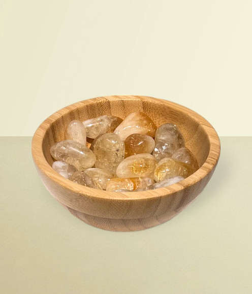 Citrine - bowl of tumbled pieces, against a warm yellow background.