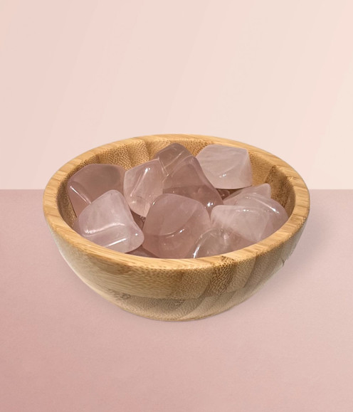 Rose Quartz - a bowl of assorted tumbled pieces, against a pale pink background.