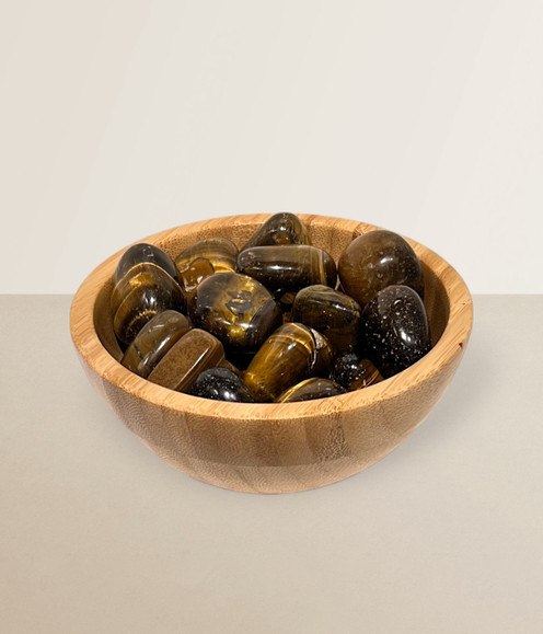 Tigers Eye - a bowl of assorted tumbled pieces, against a light brown background.