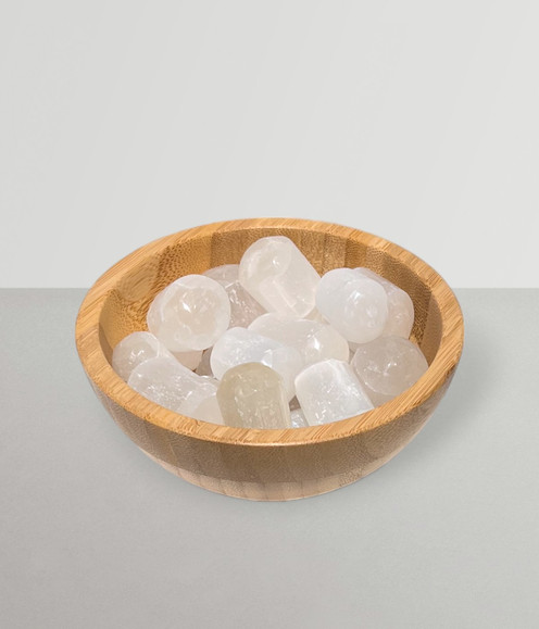 Selenite - a bowl of assorted tumbled pieces, against a pale grey background.