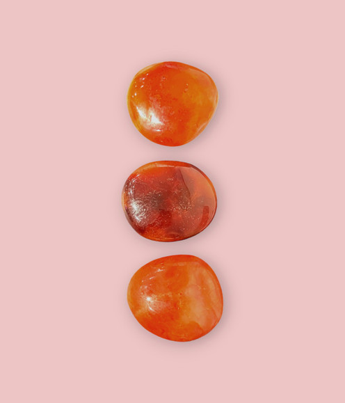 Carnelian Palm Stones - an assortment of three medium sized pieces, against a pink background.