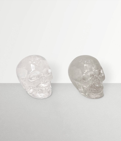 Clear Quartz Skull Carvings, two samples angled to the left side, front-facing, against a pale grey coloured background.