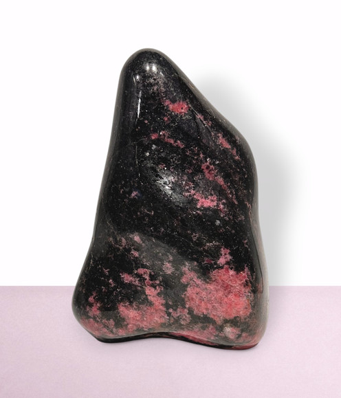 Rhodonite Free Form - solo piece #6, from the back, against a light pink coloured background. Rhodonite Free Form - solo piece #6, from the back, against a light pink coloured background.