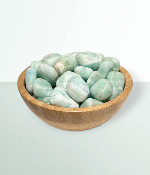 Caribbean Calcite - a bowl of assorted tumbled pieces, in a small size, against a cool blue-green coloured background.