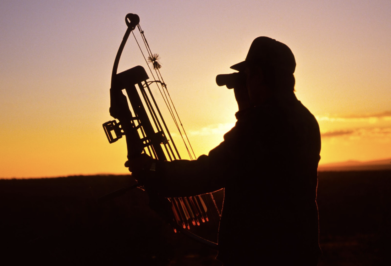 silhouette of a man hunting holding a crossbow with a sunrise in the back