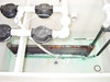 Interior of HDPE tank showing copper tubing coil, multiple black-cap fittings, PVC pipe connections, and green residue on tank bottom — overhead view
