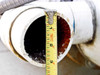 Tape measure across shell nozzle opening showing approximately 3.5 in inner diameter — rust and mineral deposits visible inside nozzle