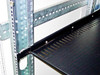 Close-up of vented black rack shelf installed on 19-inch rails inside the cabinet