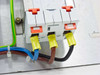 Close-up of three-pole breaker/contactor rear terminals showing red and orange tripping flags, yellow insulated ferrule connections on blue, brown, and black phase conductors