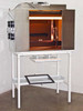 CRP L-207-B light box exposure chamber powered on with amber interior lighting, mounted on white metal table stand — front 3/4 view