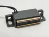 Side view of magnetic proximity reed switch showing rectangular gray housing, metallic reed contact strips, and short black lead wire exiting rear