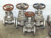 Three Powell 150-class stainless steel flanged gate valves side by side with red handwheels showing body markings