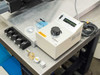 Olympus TGH illumination controller on bench — front panel showing voltage selector (2-12V), power switch, accessories including nanoindenter tip box, sample mounts, and calibration standard