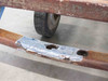 Close-up of deteriorated Cost Cutter brand plate on lower frame rail showing cracked and peeling paint and caster wheel behind it