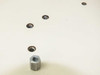 Close-up of threaded feed-through holes in steel table surface with one loose hex standoff nut shown for scale