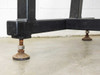 Close-up of two adjustable bolt-style leveling feet on black welded steel frame base, showing rust on leveling hardware