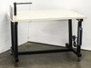 Lab tech bench work table with white steel top, black welded frame, vertical post with arm, and power strip mounted to right leg — front three-quarter view