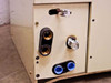 Lower corner of air handler showing refrigerant line connections — one capped copper fitting, one capped port with foil wrap, and dual blue-cap drain/line grommet; surface shows scuffing and scoring