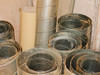 Close-up of galvanized round duct sections standing upright showing dust accumulation and surface oxidation on interior and exterior surfaces