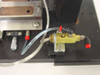 Close-up of brass pneumatic valve manifold with red-capped push-fit fittings, clear pneumatic tubing, and two cylindrical contact probes on black base