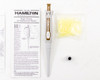 Hamilton 55019-07 single-channel fixed volume pipette showing gold-accented SoftGrip body with 50µL volume marking, alongside calibration certificate, manual, tips, and calibration tool