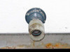 Poly tank side outlet fitting close-up — threaded hose-barb style fitting with chemical residue and rust staining on metal frame below