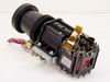 LCD projector lens assembly rear-angled view showing dichroic prism block with two LCD panels, flat flex cables, and projection lens barrel