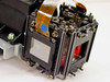 Close-up of opposite side of prism block showing two LCD panels, flat flex cables, blue sticker label, and metal frame with mounting screws