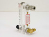 Dwyer VFA-4-SSV flow meter rear/side view showing red caution label, stainless compression fitting at top, brass NPT outlet fitting at bottom right, and model markings