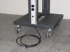 Close-up of rack base showing four swivel casters, power strip outlets on rail, and included AC power cord coiled on floor