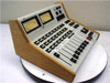 Graham Patton Systems 608 Audio Mixer – left-side 3/4 angle view showing angled console profile, wood side cheeks, faders, and button rows