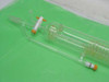 Full-length view of glass spiral coil heat exchanger alongside separate condenser or cylinder piece — both with orange/white port fittings