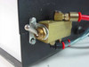 Side panel of controller enclosure showing toggle switch and brass pneumatic solenoid valve with red-capped fittings and braided tubing connections