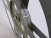 Side edge view of light gray 16mm film reel with a small roll of leader/tape wound on the hub, showing the reel profile and film gate slot