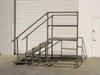 Mobile steel work platform with diamond plate steps and 42-inch safety rails on lockable casters — side angle view showing stair ascent and upper deck frame