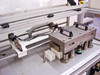 Close-up of boat shuttle tooling fixture on linear rails – showing handle-equipped metal platen, guide posts, and pneumatic actuator assembly