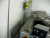 Branson TDR-15 conveyor end section – shows vertical support column, yellow warning label, control panel with red emergency stop button, and stainless steel conveyor trough below