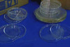 Assorted Pyrex glass petri dishes laid out — culture dishes with cross-divider lids at left, stacked larger beaker covers and watch glasses at right, some yellowing on larger pieces