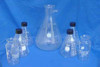 Pyrex Corning lab glassware lot — full group view showing 4x 4985 1000ml Erlenmeyer screw-top flasks, 1x large 4000ml filter flask with sidearm, and 2x 500ml Fleakers on blue background