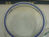 Top-down view inside Wheaton desiccator glass bowl showing circular perforated metal shelf insert resting on ledge with blue rubber gasket visible at rim