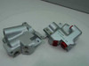 Two silver aluminum valve bodies part 14-43451-1 side by side — one with red plastic port covers, one without