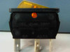 Close-up of IDEC Izumi Corp illuminated orange rocker switch, rear view showing blade terminals