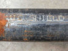 Pipe body showing MIC SHIELD lettering stenciled in white paint on black-coated steel surface with surrounding rust