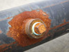 Close-up of threaded boss on pipe body showing heavy rust and corrosion around weld area with visible bolt or plug fitting